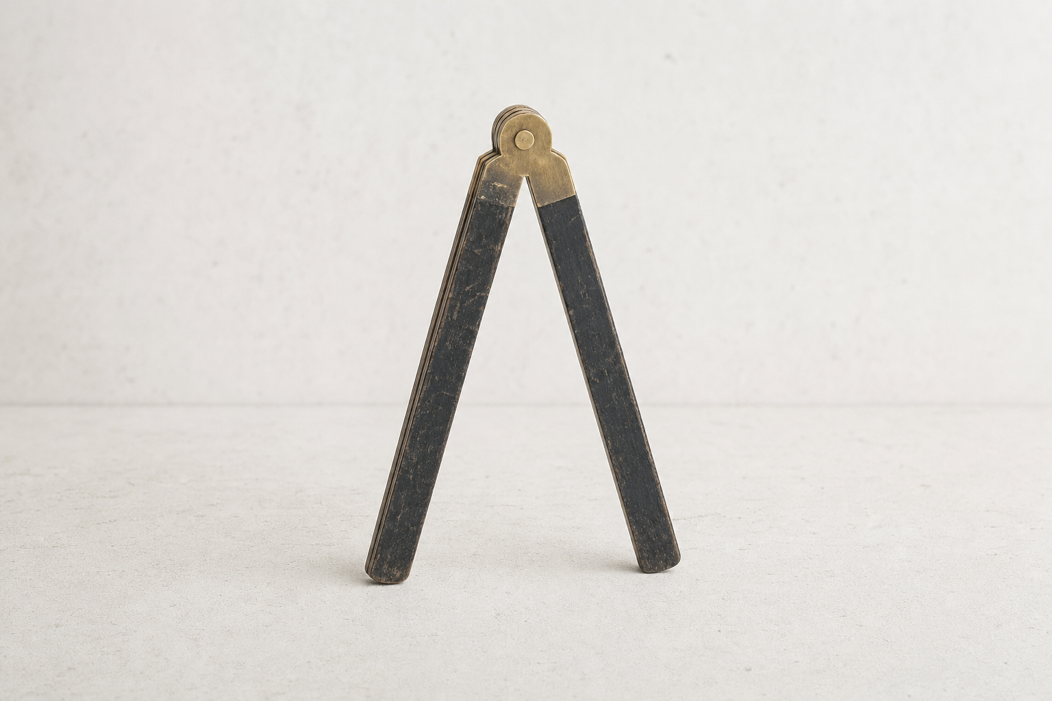 A worn dark boxwood folding rule standing part-folded like an open V on a pale surface, its marked faces turned inward